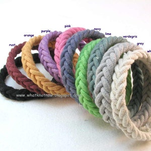 Könnte beinhalten: Ein Set aus 11 geflochtenen Baumwollschnüren in verschiedenen Farben, darunter Schwarz, Rost, Orange, Lila, Pink, Marine, Limette, Grünspan, Grau und Weiß. Die Schnüre sind fächerförmig angeordnet, wobei die schwarze Schnur unten und die weiße Schnur oben liegt.