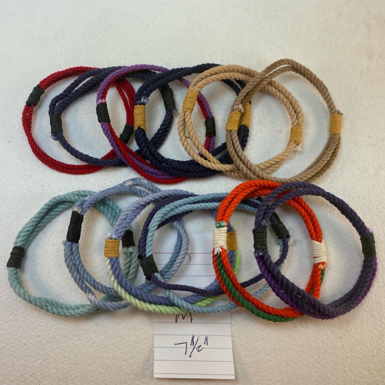 group of remainder string bracelets size medium. These bracelets are made with multiple strands of colored cotton cord bound with waxed thread whippings creating a fixed size slip on rope bracelet. A notation reading 7 1/2" is visible at the bottom of the frame