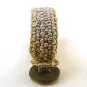 May include: A woven bracelet with a green and brown color gradient. The bracelet has a stone clasp.