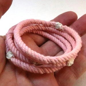Könnte beinhalten: Rosa geflochtenes Seil mit weißen Knoten. Das Seil ist aufgerollt und wird in einer Hand gehalten.