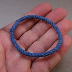 Puede incluir: Un brazalete de cuerda azul, atado en un círculo, se sostiene en la mano de una persona.