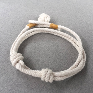 Könnte beinhalten: Ein weißes Seil-Armband mit zwei braunen Lederakzenten. Das Armband ist an beiden Enden mit einem Knoten gebunden.