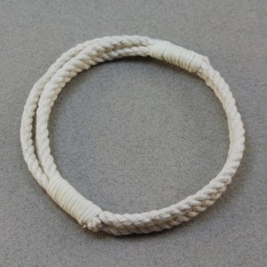 May include: An off-white rope bracelet, circular in shape. The bracelet is constructed from two parallel strands of twisted rope, secured at intervals with wrapped cord. The rope has a textured finish, and the design is simple and nautical in style.