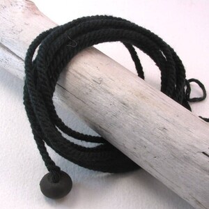 May include: A black cord with a black wooden bead at the end. The cord is wrapped around a piece of driftwood.