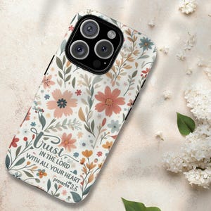 May include: A floral phone case featuring a white background with a pattern of pink, orange, and blue flowers and green leaves. The case has the text "Trust in the Lord with all your heart Proverbs 3:5".