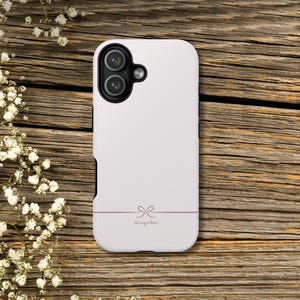 May include: White phone case with a dual-lens camera cutout. A thin, horizontal mauve line with a bow design and the text "His way is better" is centered at the bottom. The case is on a wooden surface.
