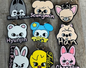 May include: A collection of eight colorful rubber keychains featuring cartoon character faces and names including Bang Chan, Seungmin, I.N., Hyunjin, Han, Lee Know, Felix, and Changbin. Each keychain has a metal lobster clasp attachment.