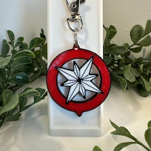 May include: A red and white keychain with a starburst design. The keychain has a silver metal clasp.