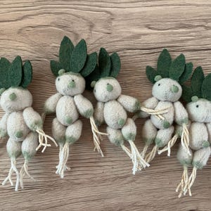 Pode incluir: Cinco plantas de brinquedo de feltro com folhas de feltro verde e corpos de feltro branco. As plantas têm um aspeto caprichoso e de desenho animado.