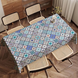May include: A rectangular tablecloth featuring a repeating geometric pattern of blue, teal, and purple tiles. The tablecloth is draped over a wooden table, with four woven chairs around it. The pattern has a vintage, Mediterranean style.