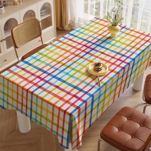 May include: A colourful checkered tablecloth with a white background and red, blue, yellow, green, and orange stripes. The tablecloth is laid out on a wooden table with two chairs.