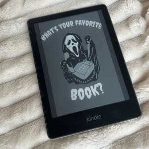 May include: A black and white illustration of Ghostface from the Scream movie franchise holding a phone and a knife. The text "What's your favorite book?" is displayed on the screen of a Kindle e-reader.