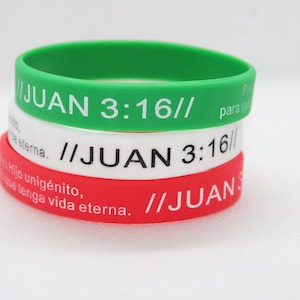 May include: Three stacked rubber wristbands in green, white, and red. Each band features the text "JUAN 3:16" in white, with additional text in Spanish. The bands are stacked on a white surface.