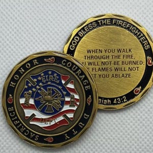 May include: A gold-colored challenge coin with a firefighter's helmet, axe, and hose on one side. The other side has the text "God Bless The Firefighters" and a Bible verse, "Isaiah 43:2".