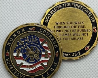 Può includere: Una moneta da sfida dorata con un elmetto da pompiere, un'ascia e una manichetta antincendio su un lato. L'altro lato ha il testo "God Bless The Firefighters" e un versetto biblico, "Isaiah 43:2".