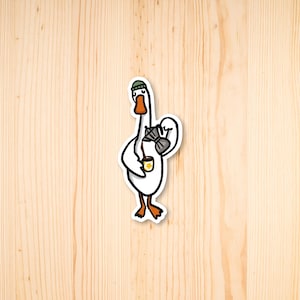 May include: A white goose wearing a green beanie and holding a cup of coffee. The goose is wearing a backpack with a brown strap.
