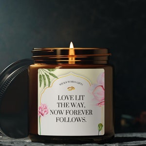 May include: A brown glass candle jar with a white label featuring a floral design and the text "LOVE LIT THE WAY, NOW FOREVER FOLLOWS."