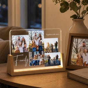 May include: A wooden-based photo display with a clear acrylic panel featuring family photos. The word "Family" is scripted on the front, and the phrase "Together, with love..." is printed on the top right. The base has a warm, glowing light.