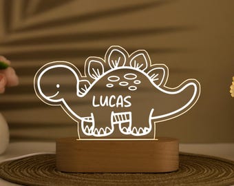 May include: A white dinosaur night light with the name "Lucas" on the side. The light is on a wooden base.