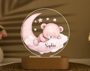 May include: A pink and white night light with a sleeping teddy bear on a crescent moon. The night light has a wooden base and the name "Sophia" is written on the moon.