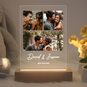 Op de afbeelding: Een houten fotolijst met een transparante acryl inzet. De lijst bevat drie foto's van een stel, met de tekst "David & Jessica Best Day Ever" onder de foto's.