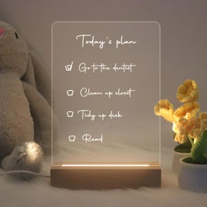 May include: A white acrylic sign with a wooden base, illuminated from below, displays a to-do list titled "Today's plan" with four items: "Go to the dentist", "Clean up closet", "Tidy up desk", and "Read".