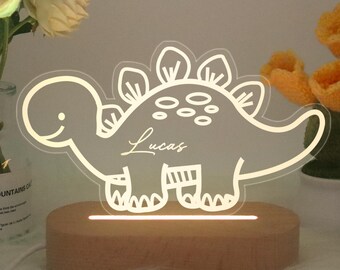 May include: A wooden night light with a white dinosaur silhouette. The dinosaur has a name, "Lucas", written on it. The light is on and illuminating the dinosaur.