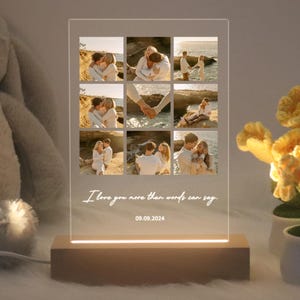 May include: A personalized acrylic photo frame with a collage of nine photos of a couple. The frame has a wooden base and a light that illuminates the photos. The text "I love you more than words can say." and the date "09.09.2024" are printed on the frame.