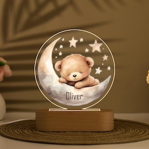 Könnte beinhalten: Eine Holz-Nachtlampe mit einem klaren Acryleinsatz, der einen schlafenden Comic-Bären auf einem Halbmond mit Sternen zeigt. Der Name "Oliver" ist auf den Mond gedruckt.