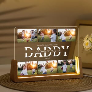 May include: A personalised acrylic photo display with a wooden base. The display features six family photos and the text "DADDY" with the names "Charles" and "Henry". The phrases "You Are The Anchor Of Our Family" and "My rock" are also included.