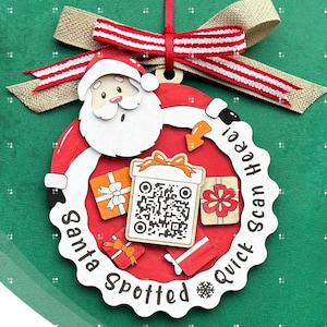 May include: A red and white Christmas ornament with a Santa Claus design. The ornament has a QR code and the text "Santa Spotted Quick Scan Here!"