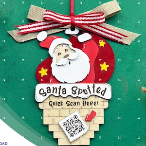 May include: A wooden Christmas ornament featuring a cartoon Santa Claus peeking out of a chimney. The ornament is decorated with red, white, and gold accents and includes the text "Santa Spotted Quick Scan Here!" and a QR code.