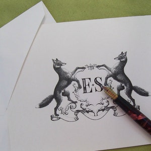 May include: A black and white illustration of two foxes flanking a crest with the initials "ES" in a decorative font. A black and red fountain pen is lying on the card.