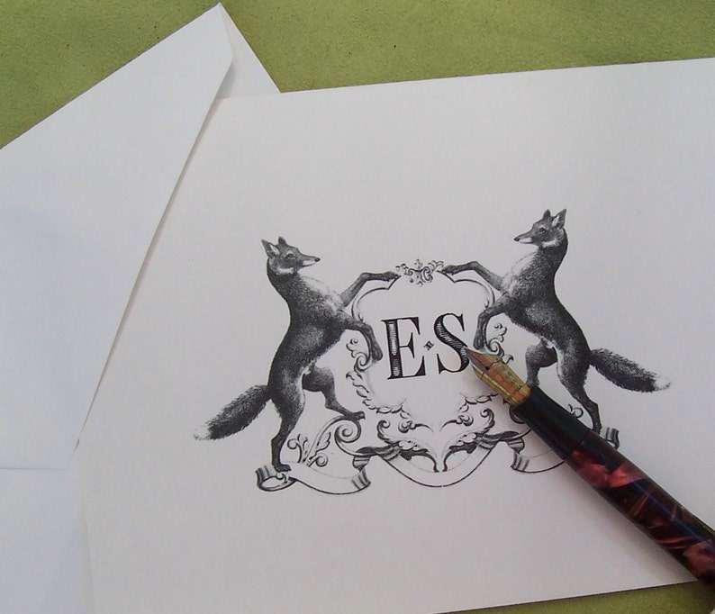 May include: A black and white illustration of two foxes flanking a crest with the initials "ES" in a decorative font. A black and red fountain pen is lying on the card.