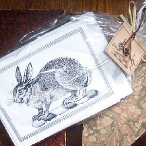 May include: A black and white illustration of a rabbit sitting on its haunches. The rabbit is drawn in a realistic style with detailed fur and whiskers.