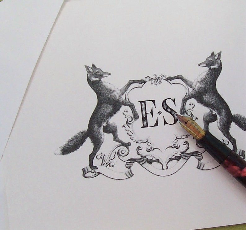 May include: A black and white illustration of two foxes flanking a crest with the initials "ES" in the centre. A vintage-style fountain pen is lying on the paper.