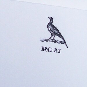 May include: A black and white illustration of a pheasant standing on a row of circles with the initials "RGM" below.