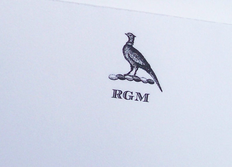 May include: A black and white illustration of a pheasant standing on a row of circles with the initials "RGM" below.