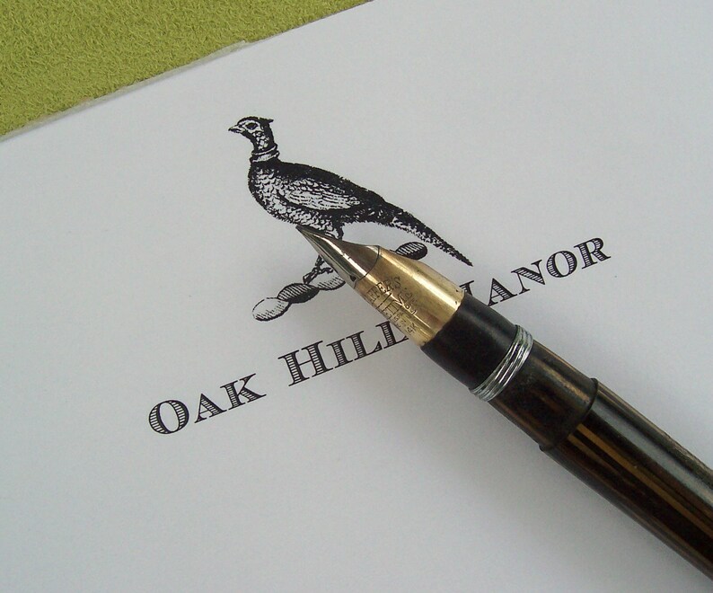 May include: A black and white illustration of a pheasant on a white card with a black fountain pen resting on the card. The card reads "Oak Hill Manor".