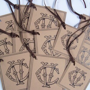 May include: A stack of brown paper gift tags with a black and white monogram design. The tags are tied with brown ribbon.
