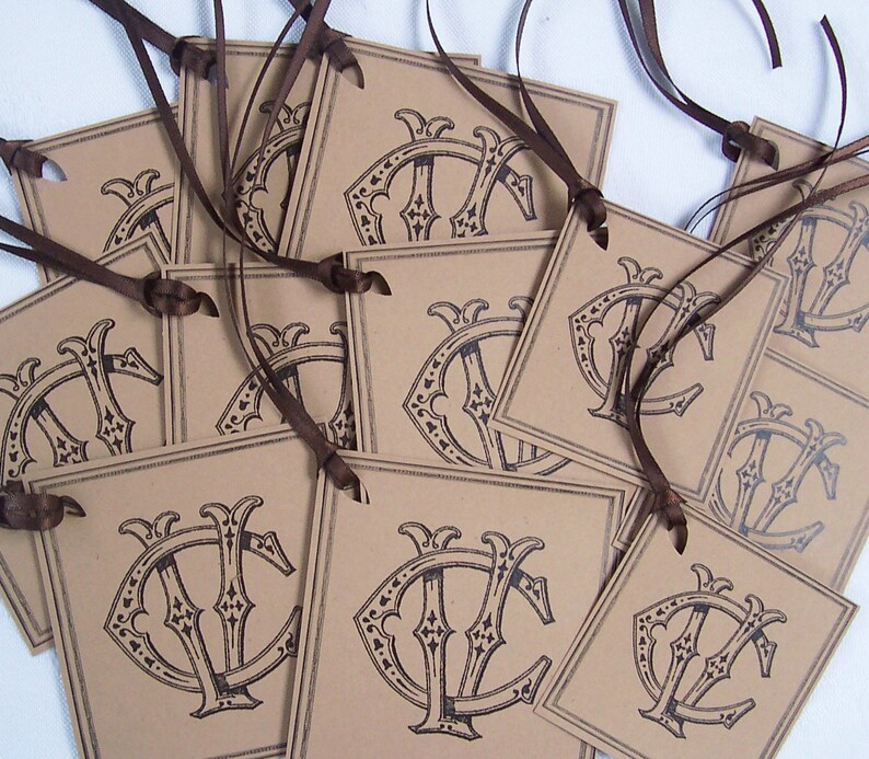 May include: A stack of brown paper gift tags with a black and white monogram design. The tags are tied with brown ribbon.