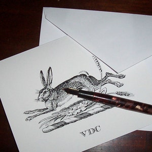 May include: Black and white illustration of a rabbit with a pen on a white card with the text "VDC" printed on it.