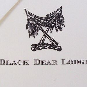 May include: Black and white illustration of two pine trees crossed over each other with the text "Black Bear Lodge" below.