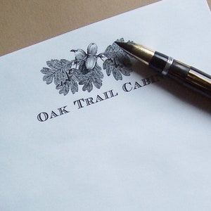 May include: White stationery with a black and white illustration of oak leaves and acorns. The text "OAK TRAIL CABIN" is printed in black.
