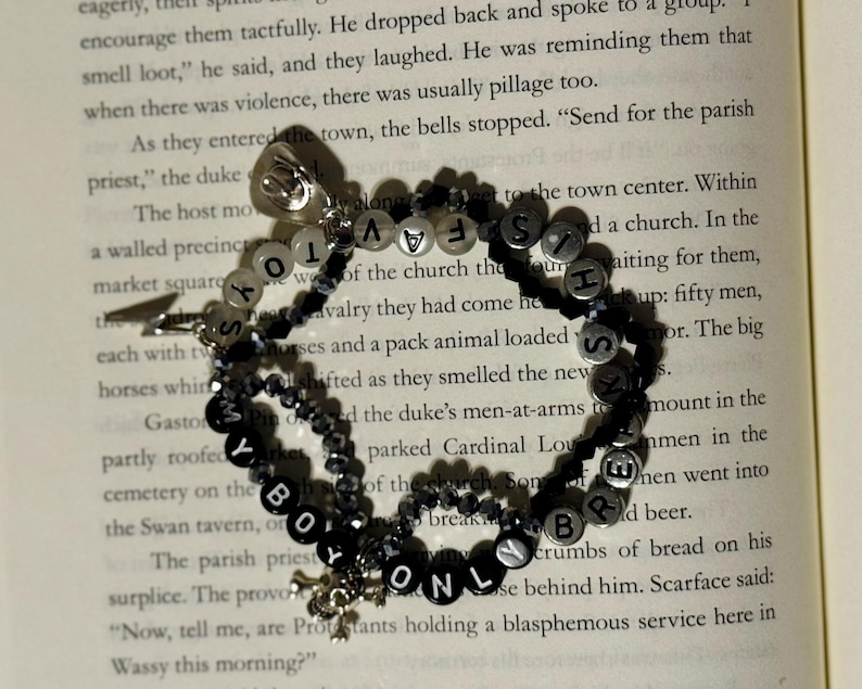 May include: A multi-strand beaded bracelet featuring black and white letter beads spelling out the phrase MY BOY ONLY BREAKS HIS TOYS. The bracelet includes small faceted black beads, silver-toned metal charms, and a small silver-toned lightning bolt charm.