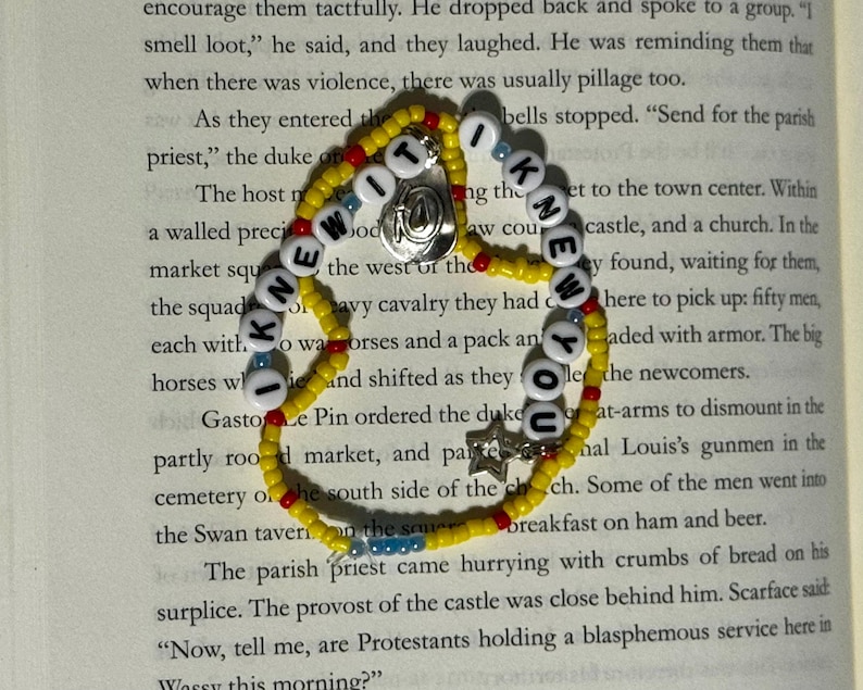 May include: A beaded bracelet featuring yellow, red, and blue seed beads with white letter beads spelling out I KNEW IT I KNEW YOU. The bracelet includes a silver-toned circular charm and a small silver-toned star charm attached to the strand.