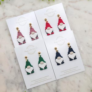 May include: Four pairs of polymer clay gnome earrings on white cards. The gnomes are in red, pink, green, and blue. The cards have the text "Happy Little Clay Co" and "Handmade Polymer Clay Jewelry".