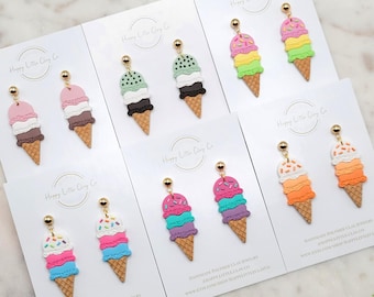 Puede incluir: Pendientes artesanales de arcilla polimérica con forma de cucuruchos de helado. Cada par presenta una combinación de colores única, incluyendo rosa, verde, azul y naranja, con postes dorados. Los pendientes se exhiben en tarjetas blancas.