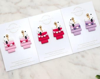 May include: Three pairs of handmade polymer clay earrings displayed on white cards. Each pair features a white koala bear design atop a tiered structure in shades of pink, red, and purple. Gold-colored earring posts are visible.