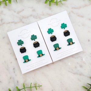 Puede incluir: Dos tarjetas blancas con diseños de trébol verde, olla de oro y sombrero de duende. Las tarjetas tienen el texto "Happy Little Clay Co." y "Aretes de arcilla polimérica hechos a mano #HappyLittleClayCo www.etsy.com/shop/HappyLittleClayCo"